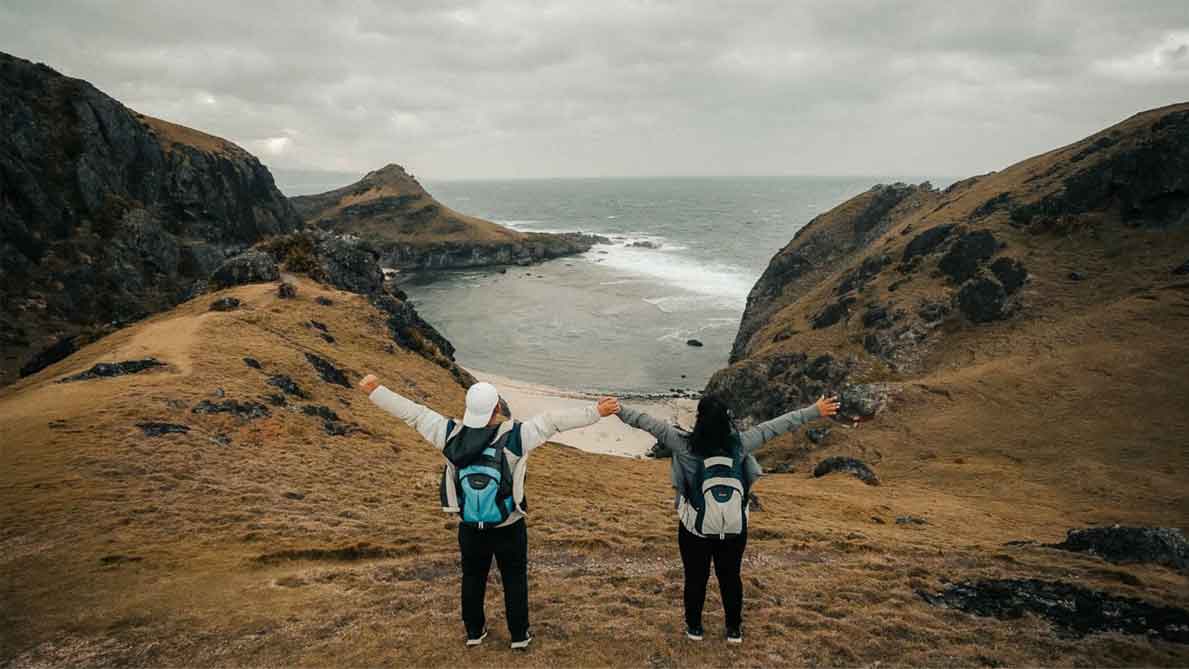 man and woman by the beach and some hills