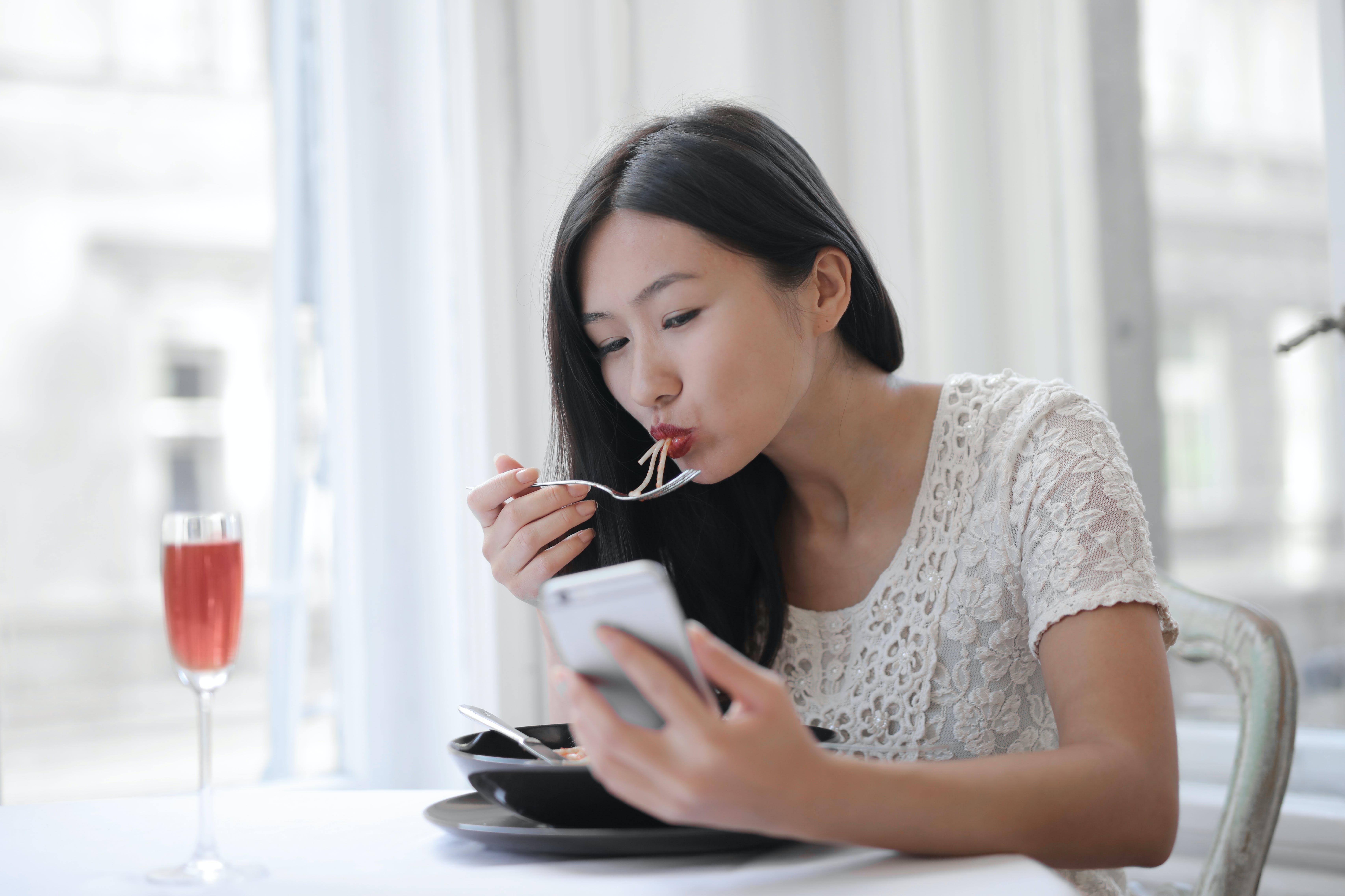 A woman eating while using her phone.