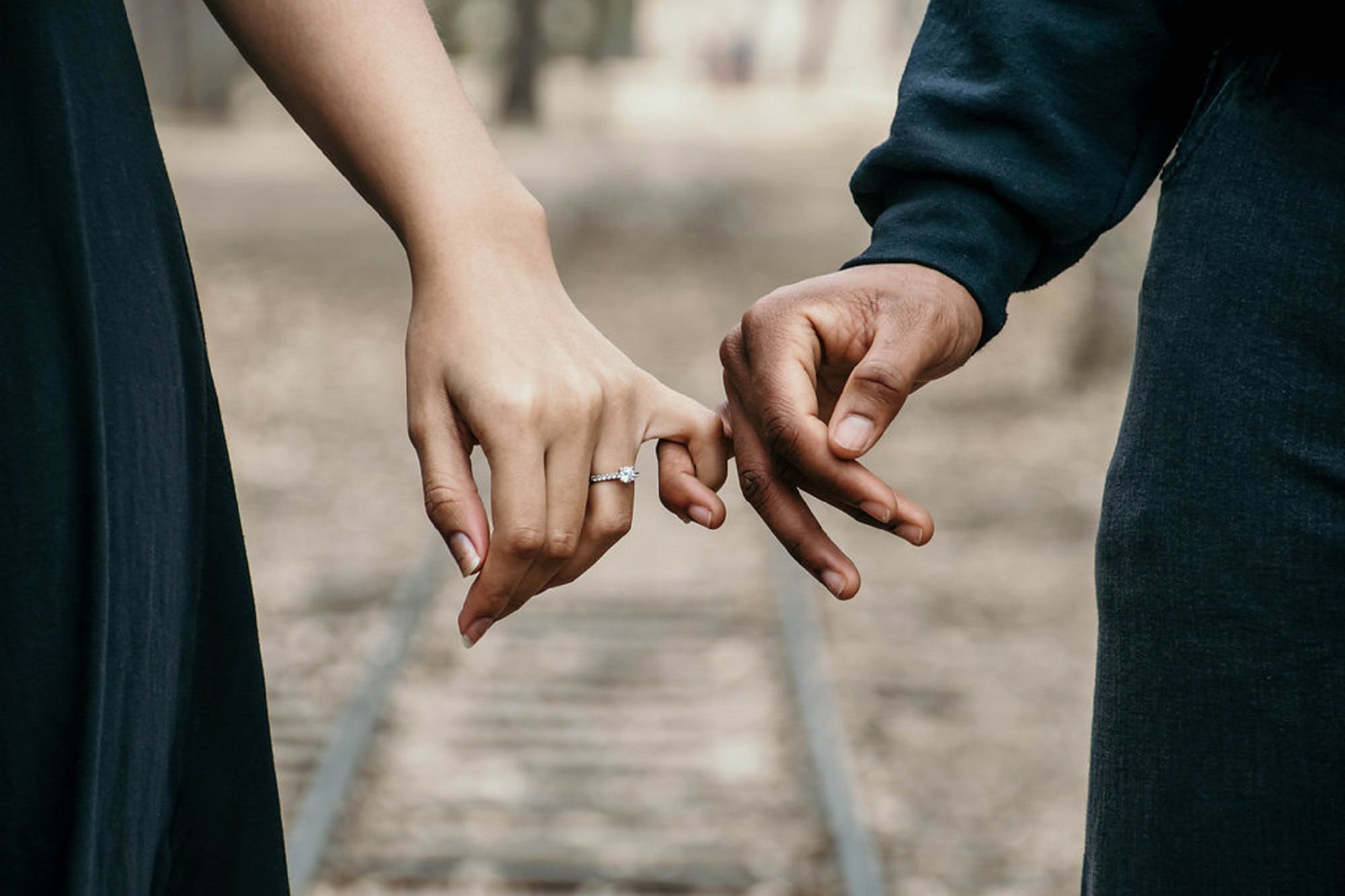 The hands of a man and a woman with their pinkies intertwined.
